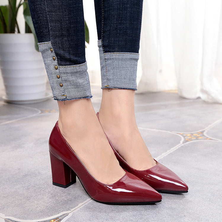 Red high-heeled shoes worn with rolled-up jeans on a light floor.