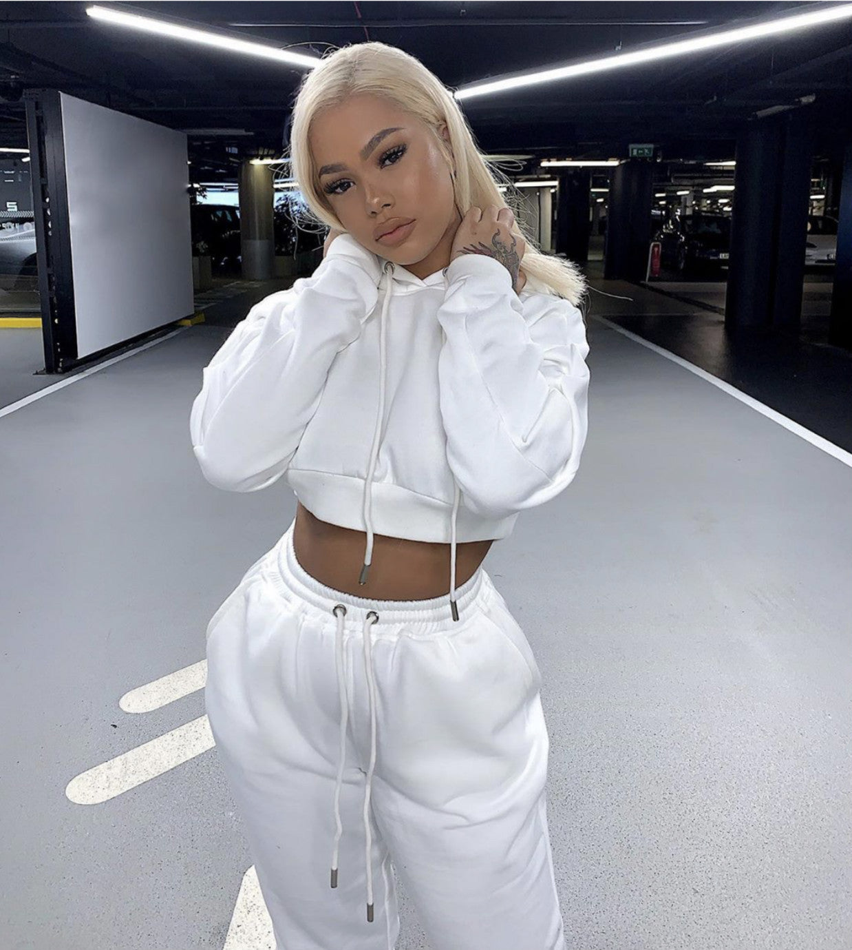 Person wearing a white hoodie and pants in a parking garage