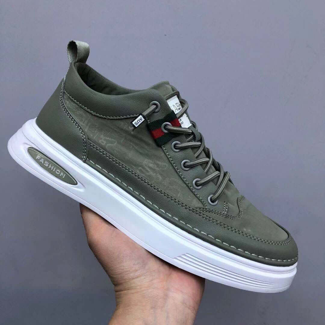 Green sneaker with white sole held by a hand against a gray background