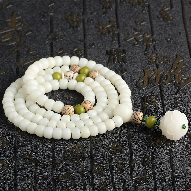 White beaded necklace with green and brown accents on a textured black background