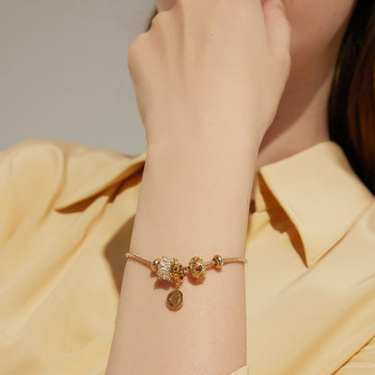 Gold bracelet with charms on a wrist against a neutral background