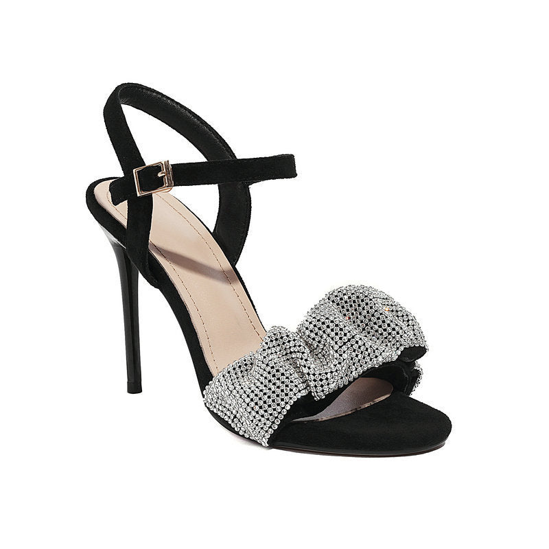 Black high-heeled sandal with a silver bow on a white background