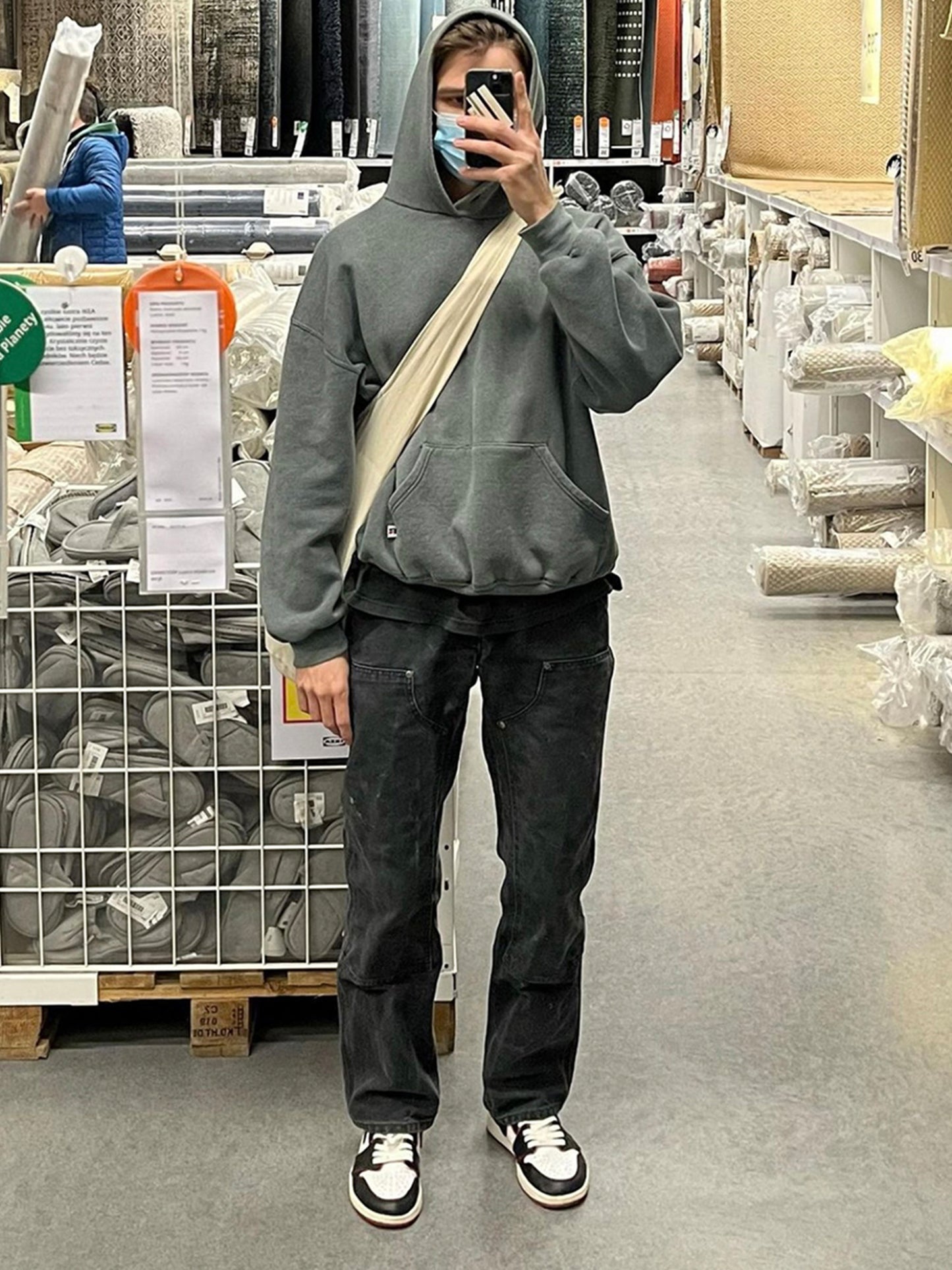 Person taking a mirror selfie in a store aisle wearing a gray hoodie and dark pants.