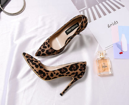 Leopard print high heels on a white surface with a magazine and perfume bottle.