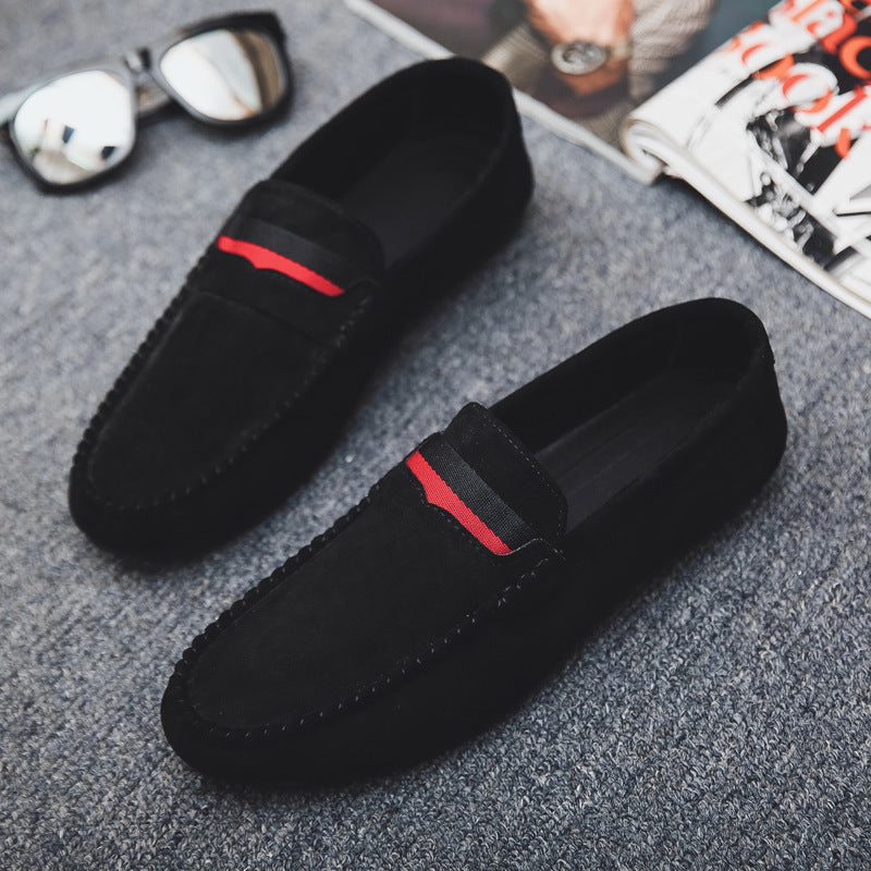 Black loafers with red accents on a gray surface, with sunglasses and a magazine in the background.