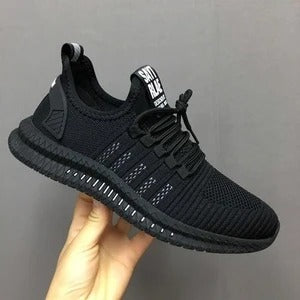 Black athletic shoe held in a hand against a gray background
