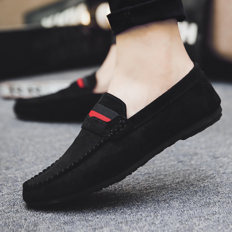 Black loafers with a red and gray strap on a gray surface