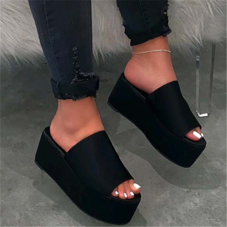 Black platform sandals worn with rolled-up jeans on a gray floor.