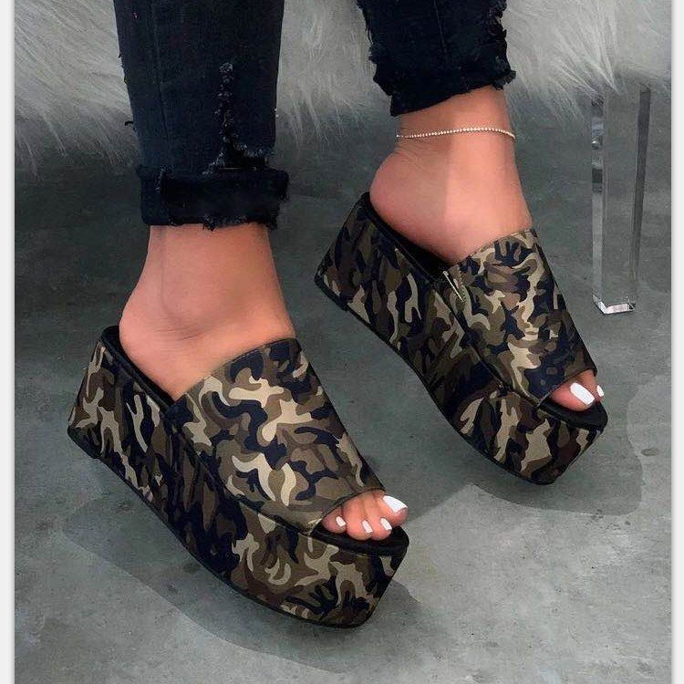 Camouflage platform sandals worn with black jeans on a gray floor.