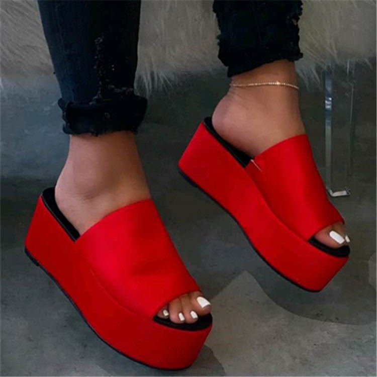 Red platform sandals worn with black pants on a neutral background