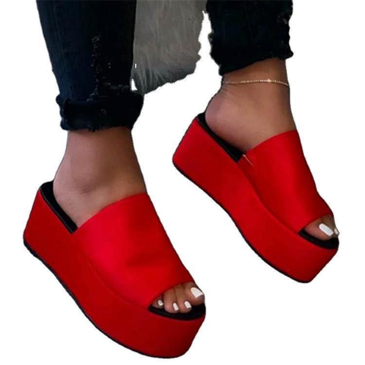 Red platform sandals worn with black pants on a white background