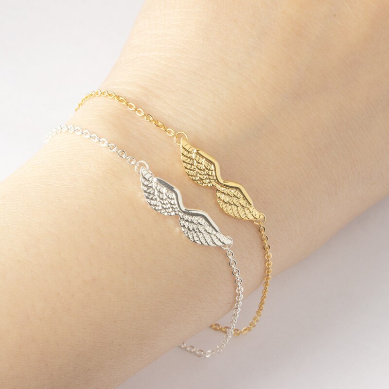 Gold and silver angel wing bracelet on a wrist against a neutral background