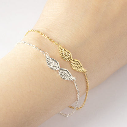 Gold and silver angel wing bracelet on a wrist against a neutral background