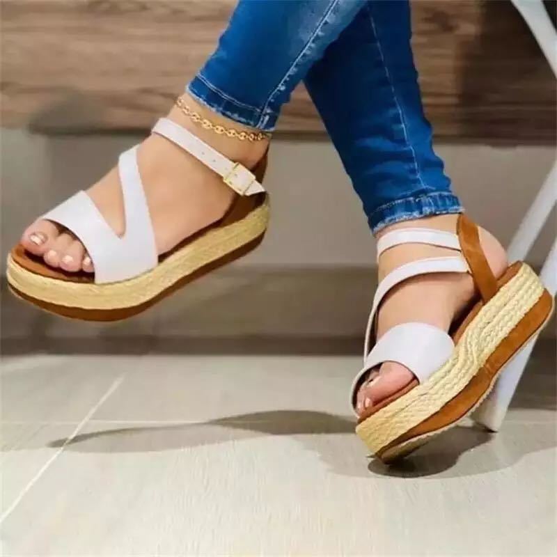 White sandals with brown soles worn by a person on a neutral background