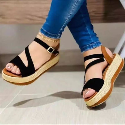 Black sandals with brown soles worn by a person on a light wooden floor.