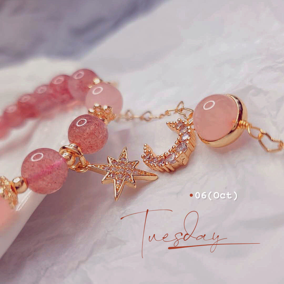 Bracelet with pink beads and gold accents on a marble surface, featuring the word 'Tuesday'.