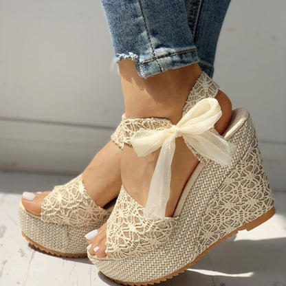 Beige lace wedge sandals with a bow on a neutral background