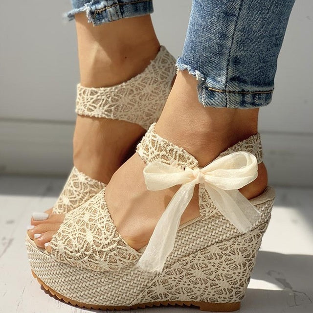 Beige lace wedge sandals with a bow on a light background