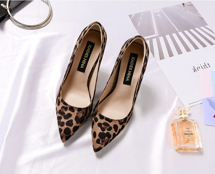 Leopard print high heels on a white surface with a perfume bottle and magazine.