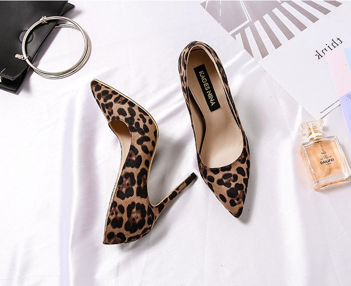 Leopard print high heels on a white surface with a handbag and perfume bottle.