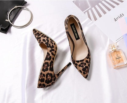 Leopard print high heels on a white surface with a handbag and perfume bottle.