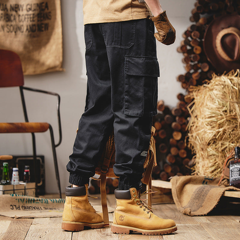 Person wearing black cargo pants and yellow boots in a rustic setting with hay and wooden elements.