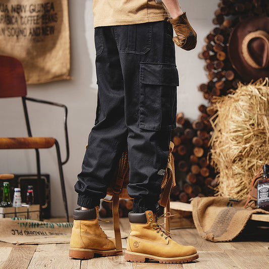Person wearing black cargo pants and yellow boots in a rustic setting with hay and wooden elements.