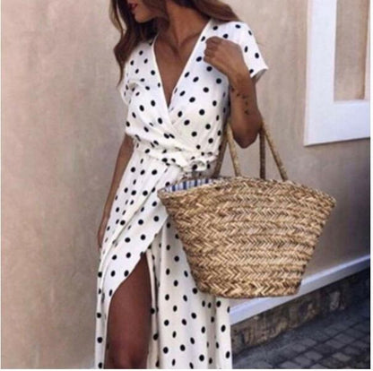 Woman in a white polka dot dress holding a straw bag against a neutral background