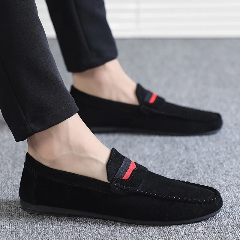 Black loafers with a red accent worn by a person on a gray floor.