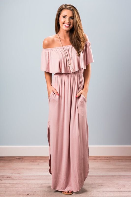 Woman wearing a pink off-shoulder maxi dress against a light blue wall.