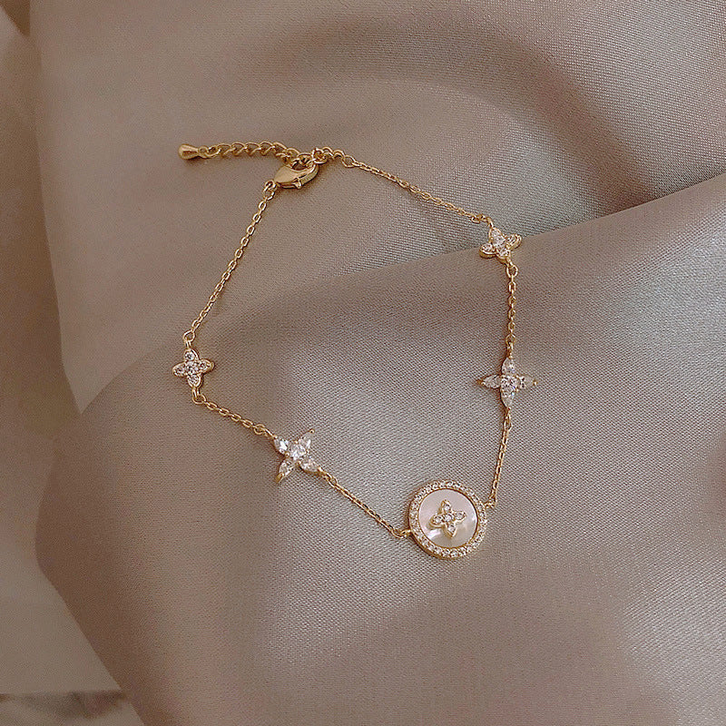 Gold bracelet with floral and circular designs on a beige fabric background