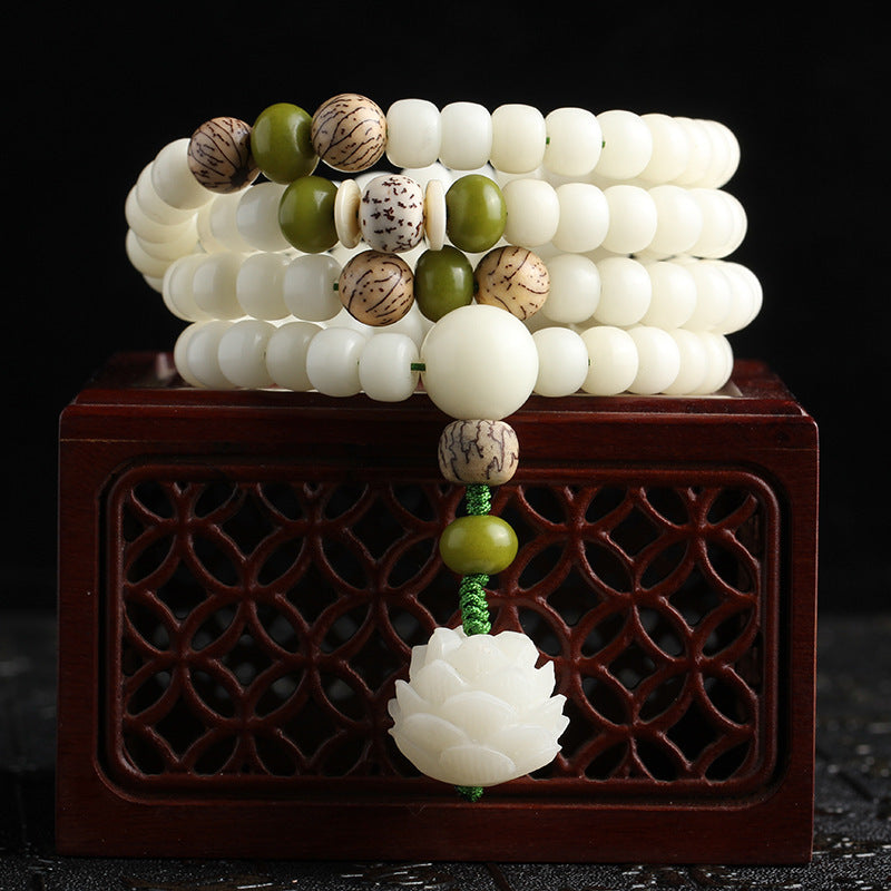 Stack of white and green beaded bracelets on a wooden box with a dark background