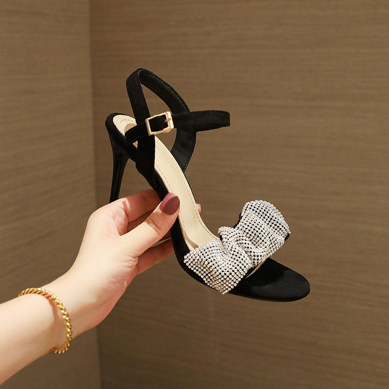 Black sandal with pearl embellishments held by a hand against a brown background