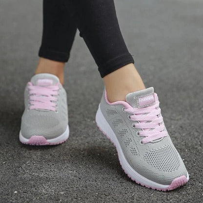 Gray sneakers with pink laces worn on a gray pavement background