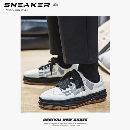White sneakers with black and brown accents worn with black pants on a light wooden floor.