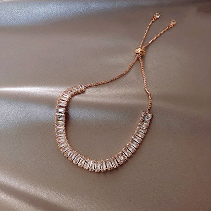 Rose gold bracelet with clear gemstones on a beige fabric background