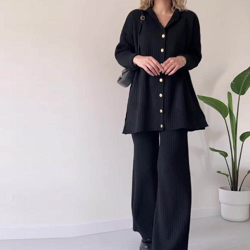 Person wearing a black outfit with white buttons in a minimal indoor setting.