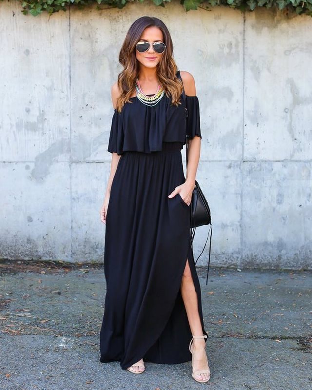 Woman wearing a black off-shoulder dress with a high slit, standing against a concrete wall.