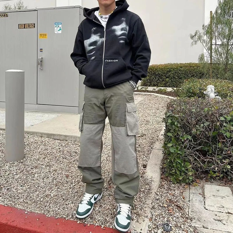 Person wearing a black hoodie with reflective design and cargo pants standing outdoors.