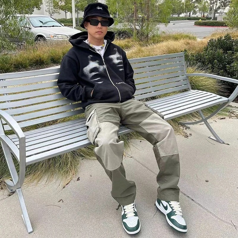 Person sitting on a bench wearing a black hoodie with white designs, beige pants, and green sneakers.