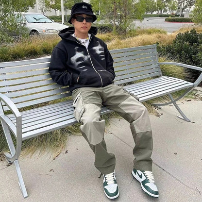 Person sitting on a bench wearing a black hoodie with white designs, beige pants, and green sneakers.