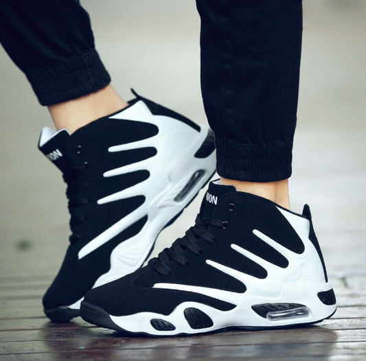 Black and white sneakers worn with black pants on a wooden floor.