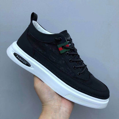 Black sneaker with a white sole held by a hand against a gray background