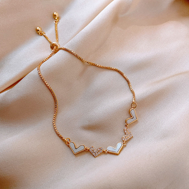 Gold bracelet with heart-shaped charms on a beige fabric background