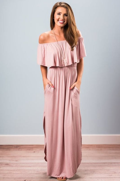 Woman wearing a pink off-shoulder maxi dress against a light gray background