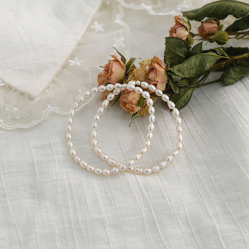 Two pearl necklaces on a textured white surface with a small bouquet of flowers.