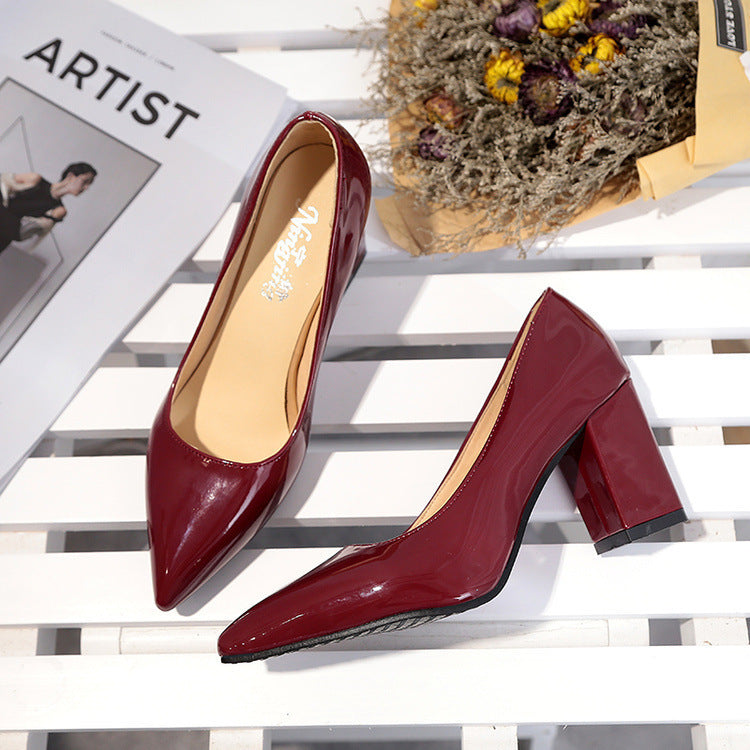 Pair of red high-heeled shoes on a white surface with a magazine and dried flowers in the background.