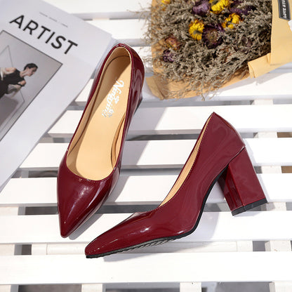 Pair of red high-heeled shoes on a white surface with a magazine and dried flowers in the background.