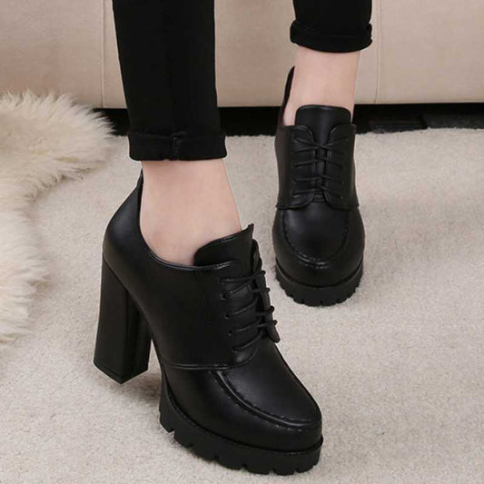 Black platform shoes with high heels worn indoors on a neutral background
