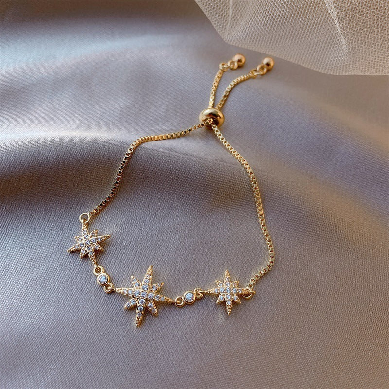Gold bracelet with star-shaped charms on a soft fabric background